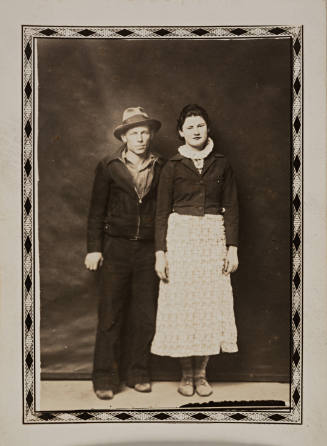 Man in hat, zippered jacket, and woman in sweater, both standing