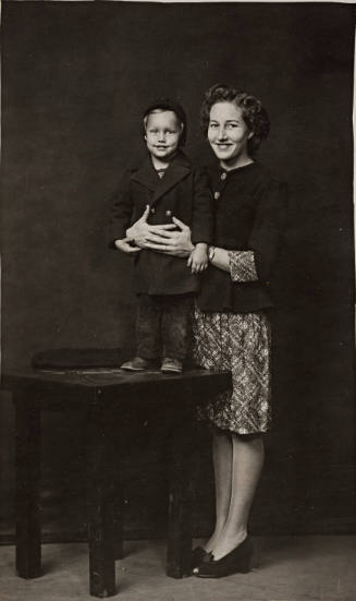Woman with arms around child on table, both wearing coats