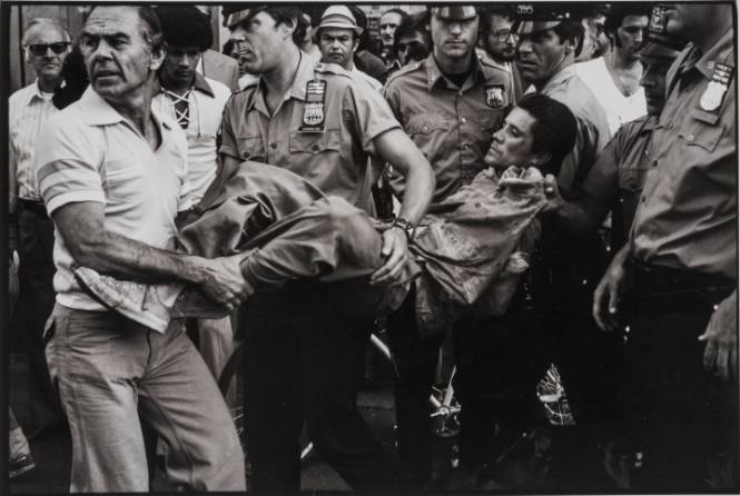 Subdued, the man is carried away in a straightjacket