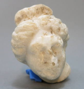 Small head of Aphrodite (?) her hair bound in large chignon at neck, and topknot on top of head