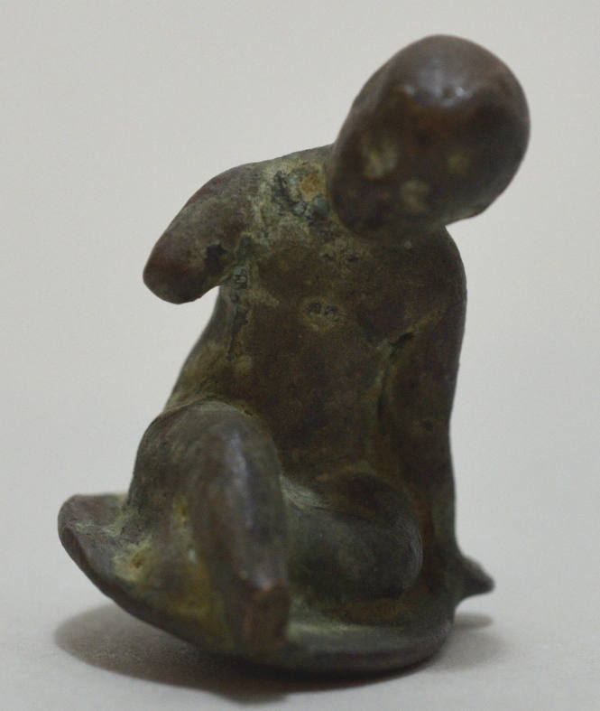 Small figure of a boy sitting on the ground, a pendant loop behind