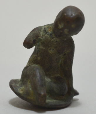 Small figure of a boy sitting on the ground, a pendant loop behind