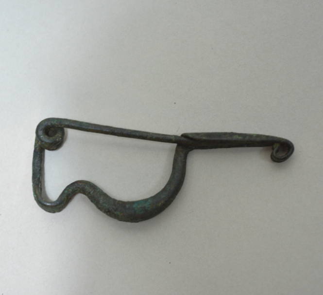 Fibula with double spiral spring; elongated catch; humped bow, and incised ornament: two horizontal bands of herringbone on bow