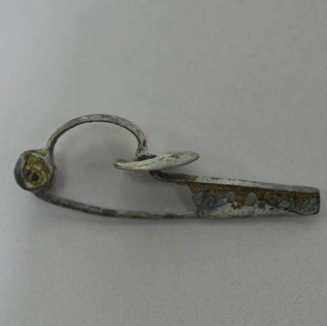 Fibula with six spiral spring, bow and tongue of flattened bronze, flat disc threaded on bow and catch with two perforations