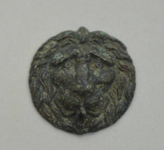 Circular applique with head of a lion in relief