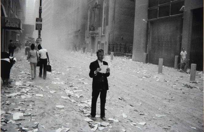 [Man reads a piece of paper in ashen street]